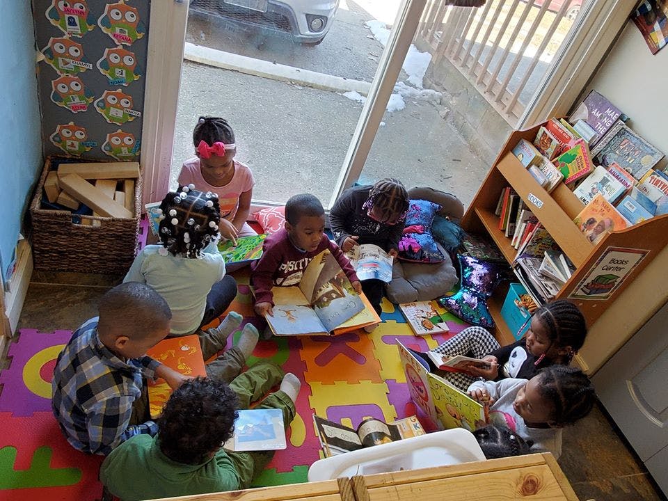 Children sitting on a colorful mat reading books in a classroom