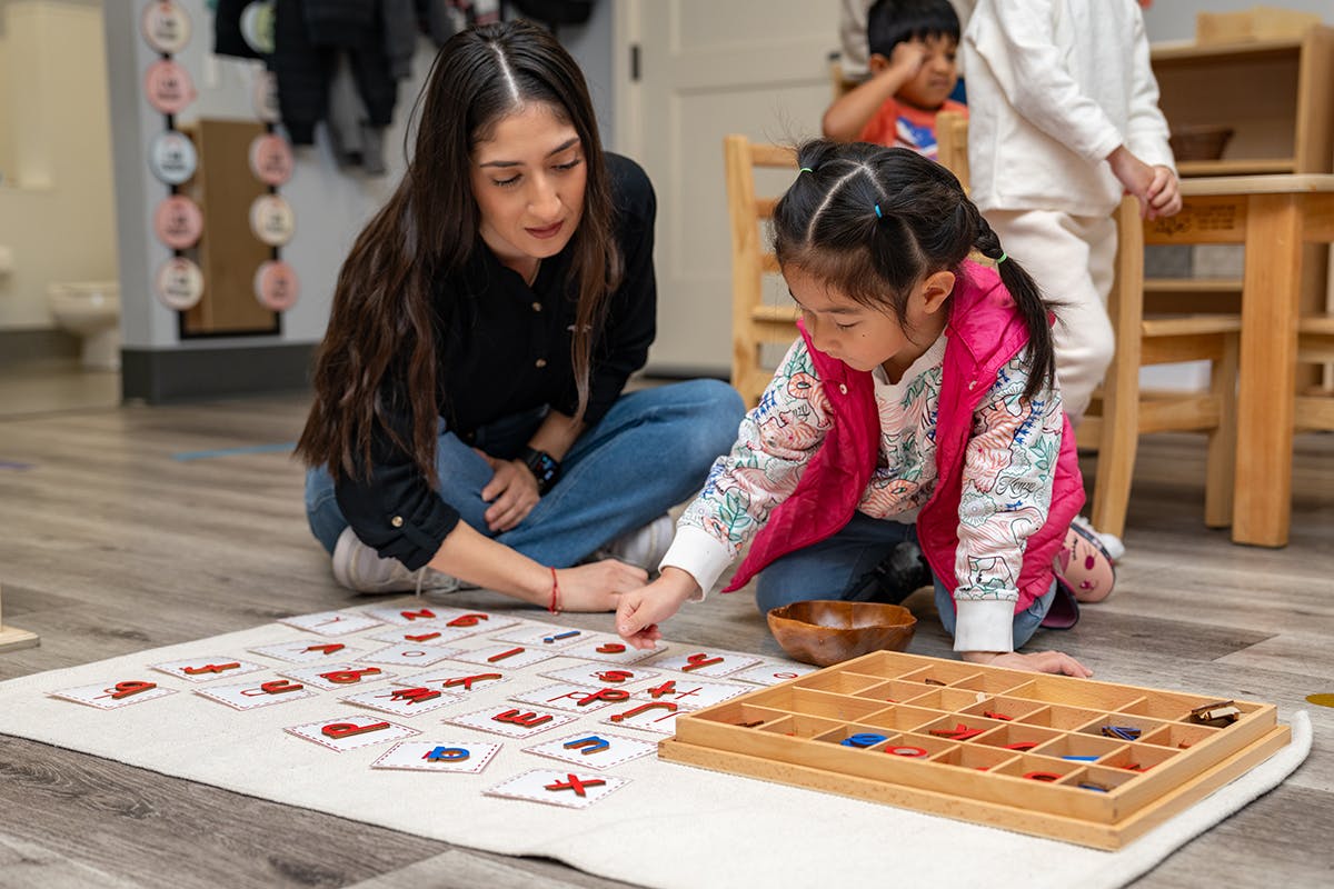 Adult and child on floor playing with letter cards and wooden tray