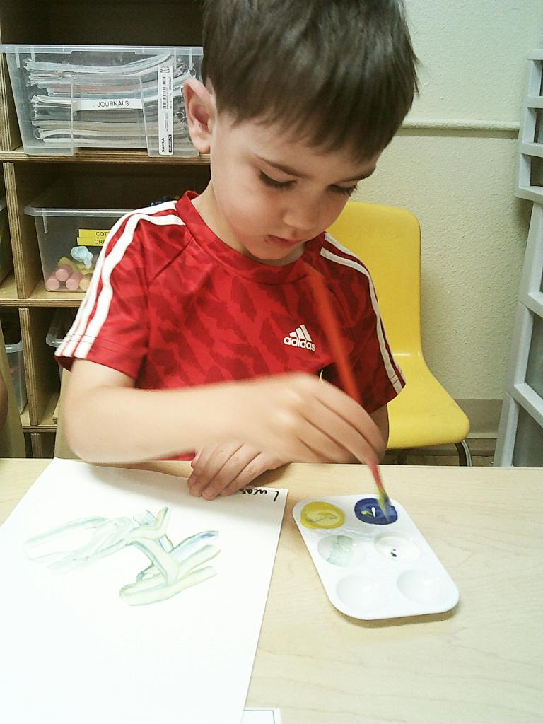 Child painting on paper with a watercolor palette in a classroom