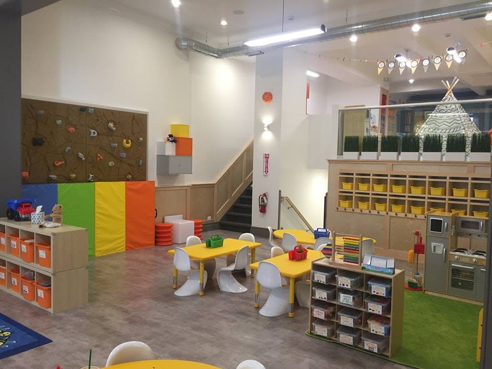 Indoor play area with small tables and chairs, climbing wall, and storage units