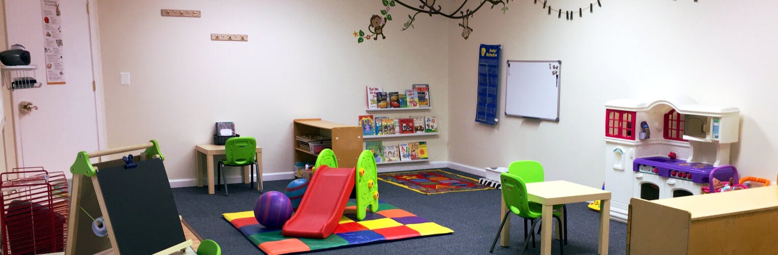 Playroom with a small slide, tables, chairs, and shelves with toys