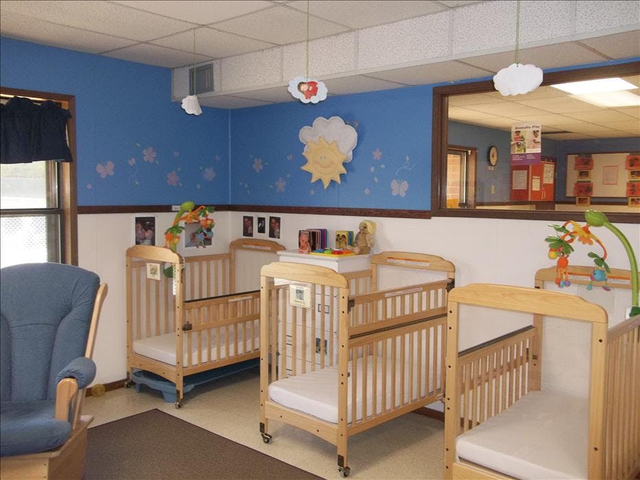 Cribs in a daycare room with blue walls, a window, and a rocking chair