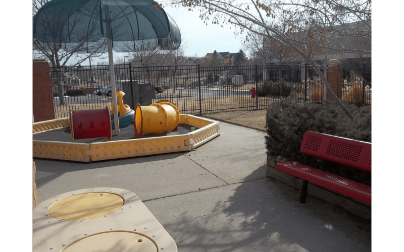 Playground area with sandpit, play equipment, and red bench