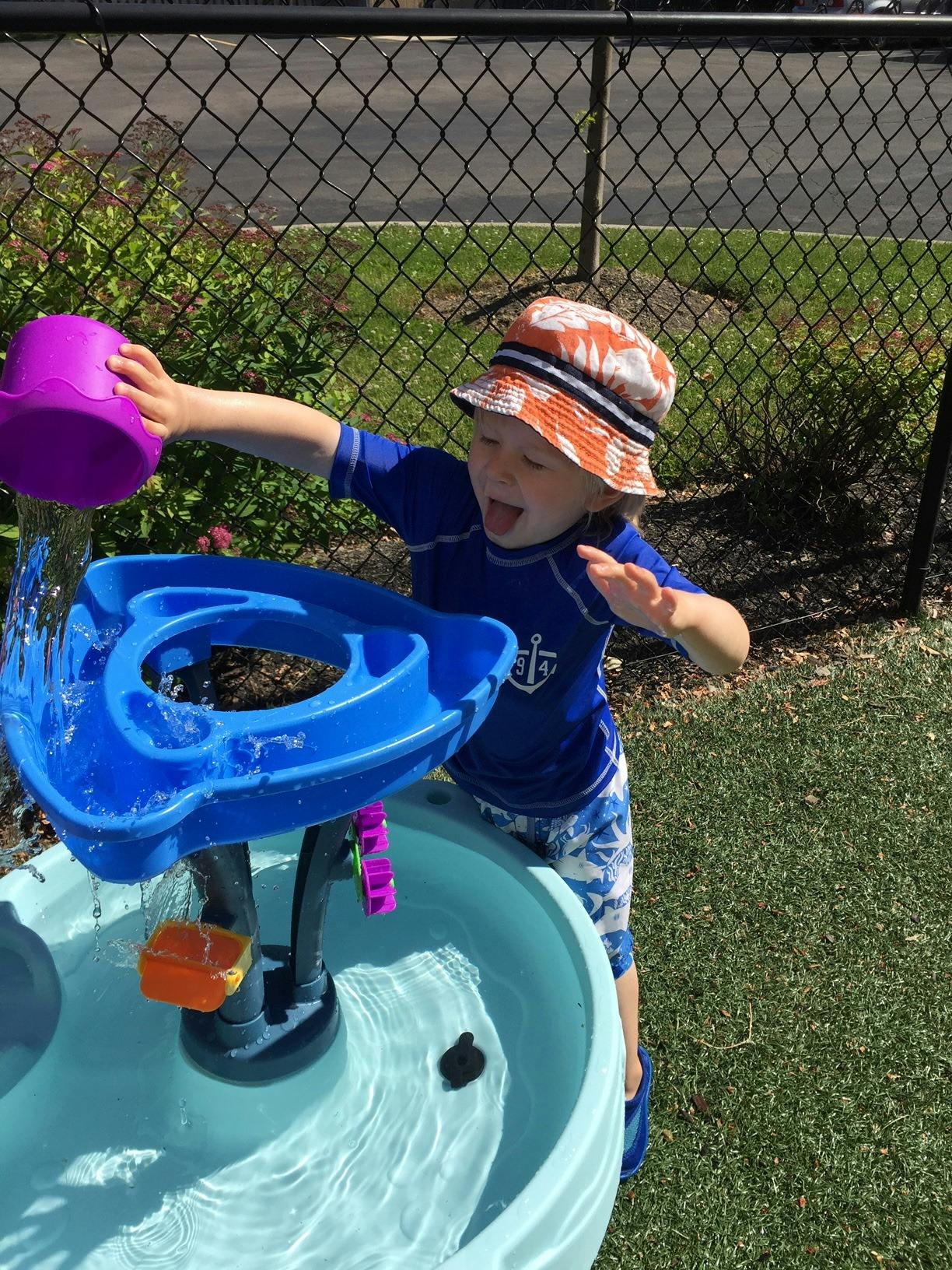 Child in a hat pouring water into a water table