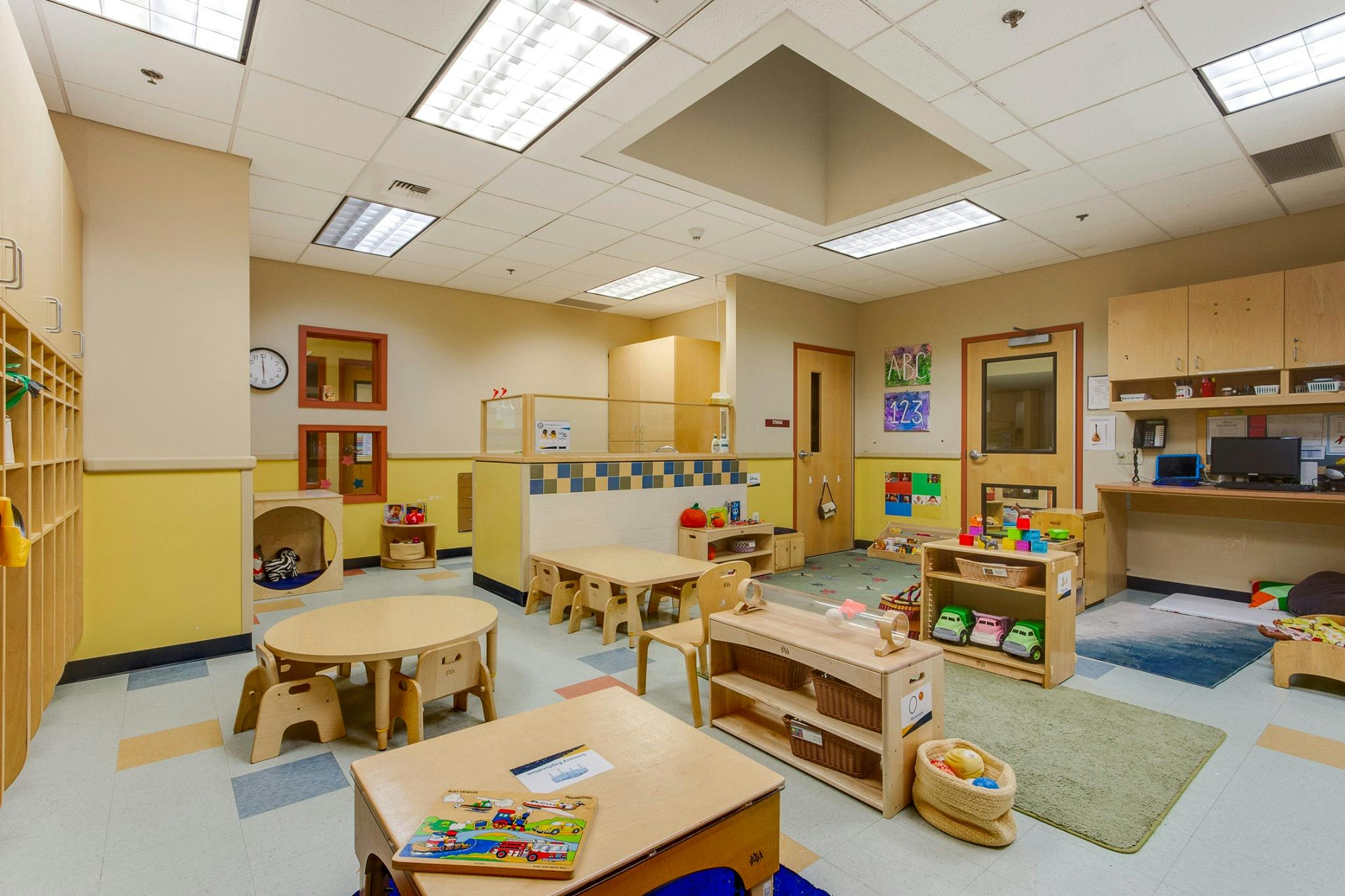 Empty classroom with small tables and chairs, shelves with toys