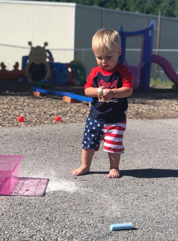 Child holding chalk over a chalk drawing on pavement
