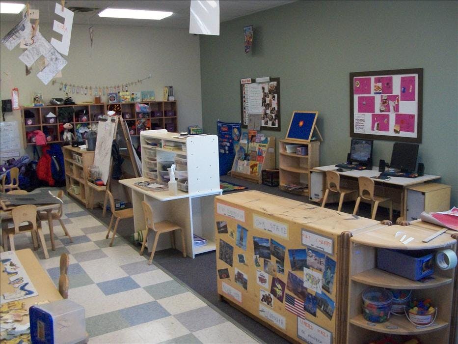 Classroom with small tables, chairs, shelving units, computers, and art on walls