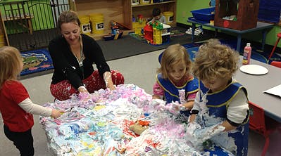 Adult and three children playing with colorful foam in a classroom