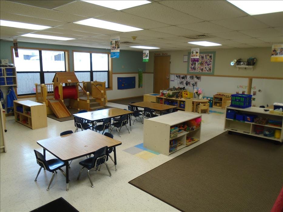 Classroom with small tables and chairs, play structure, and storage shelves
