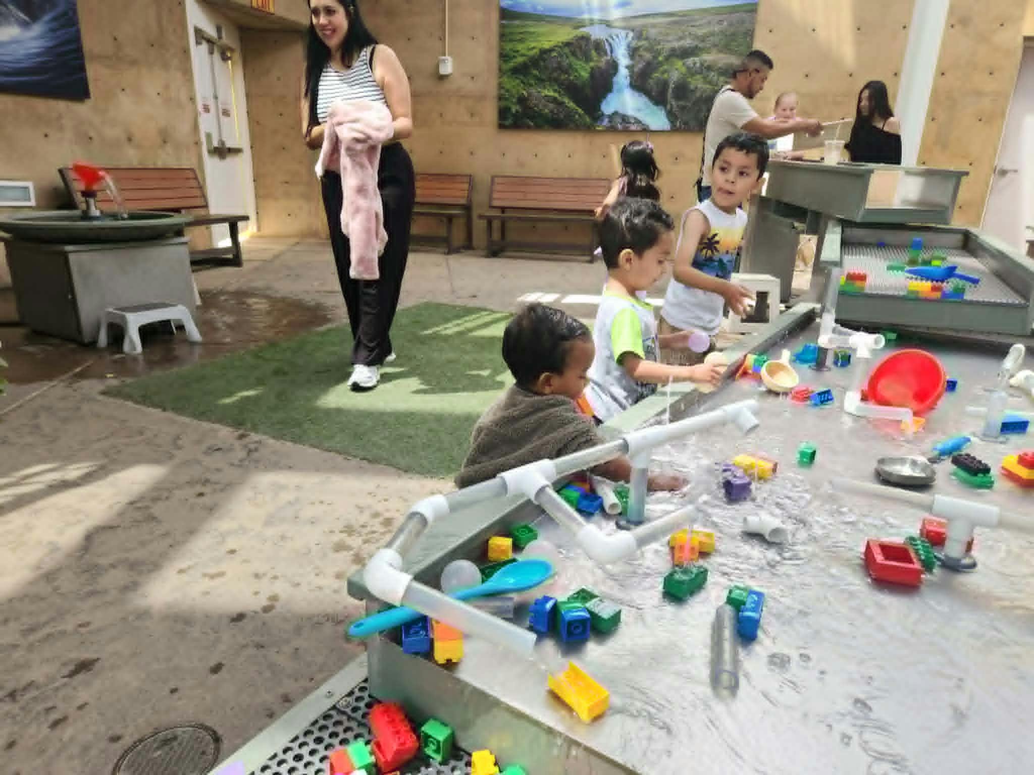 Adults and children playing at a water table with colorful toys