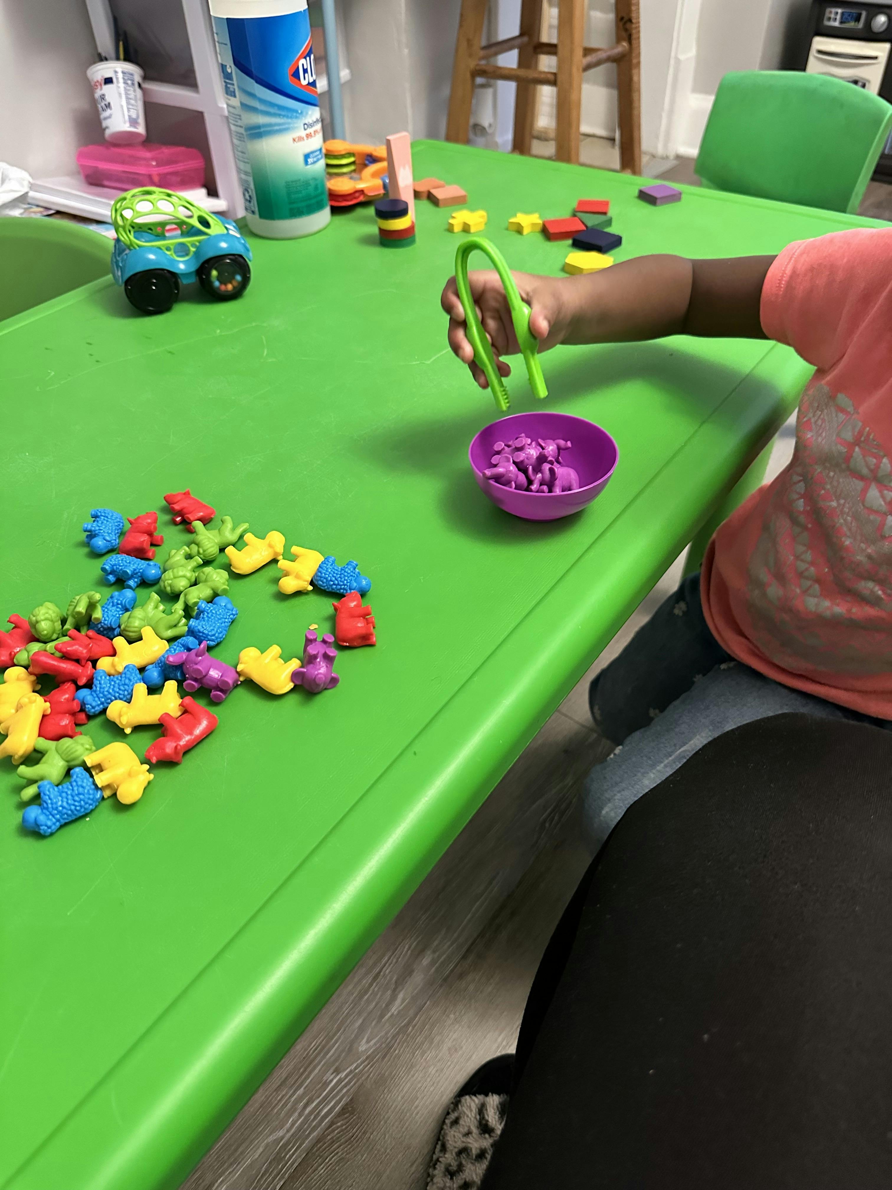 Child using tweezers to place small animal figurines into a bowl