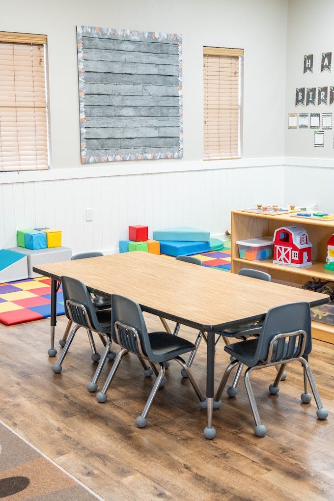 Classroom with a table and chairs surrounded by colorful play mats and toys