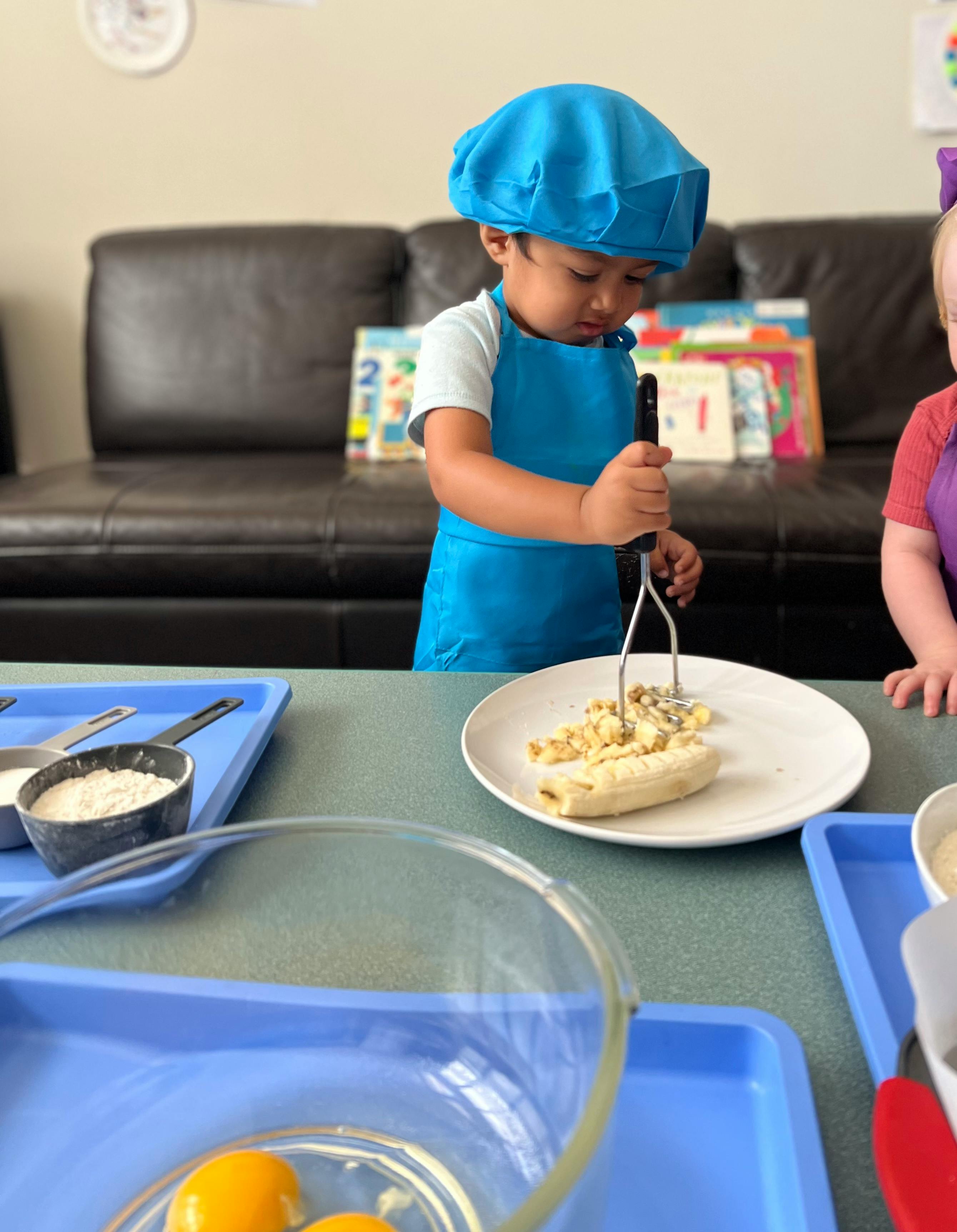 Child in chef hat and apron mashing banana on a plate