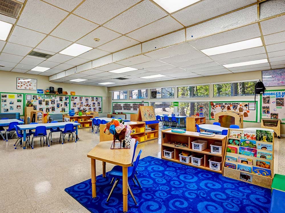 Empty classroom with small tables and chairs, shelves with toys and books