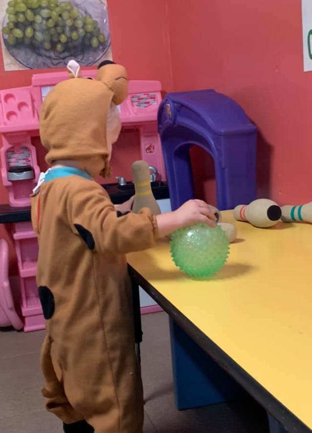 Child in costume playing with a green ball on a yellow table