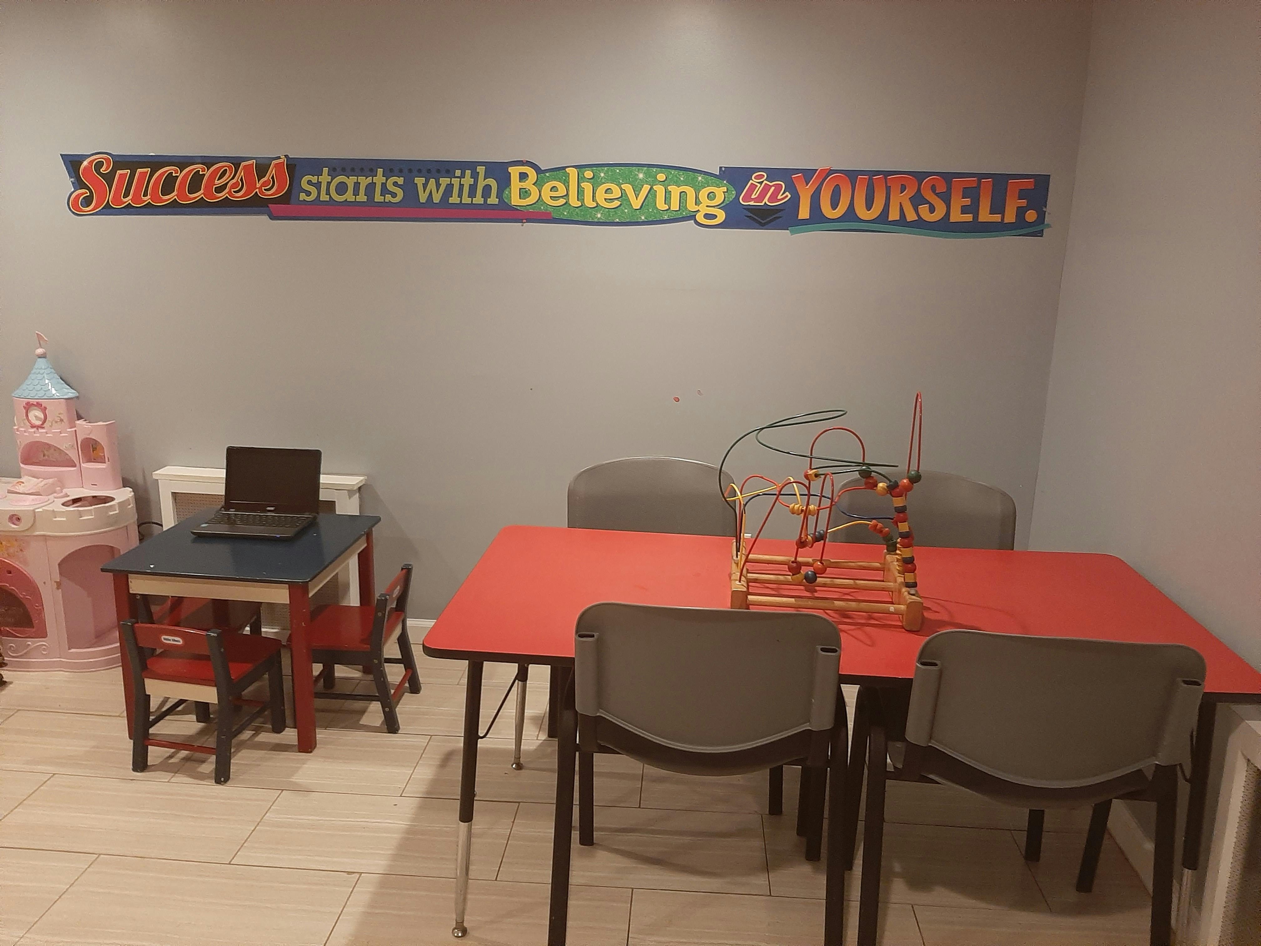 Classroom with tables, chairs, and a sign that reads "Success starts with Believing in YOURSELF"