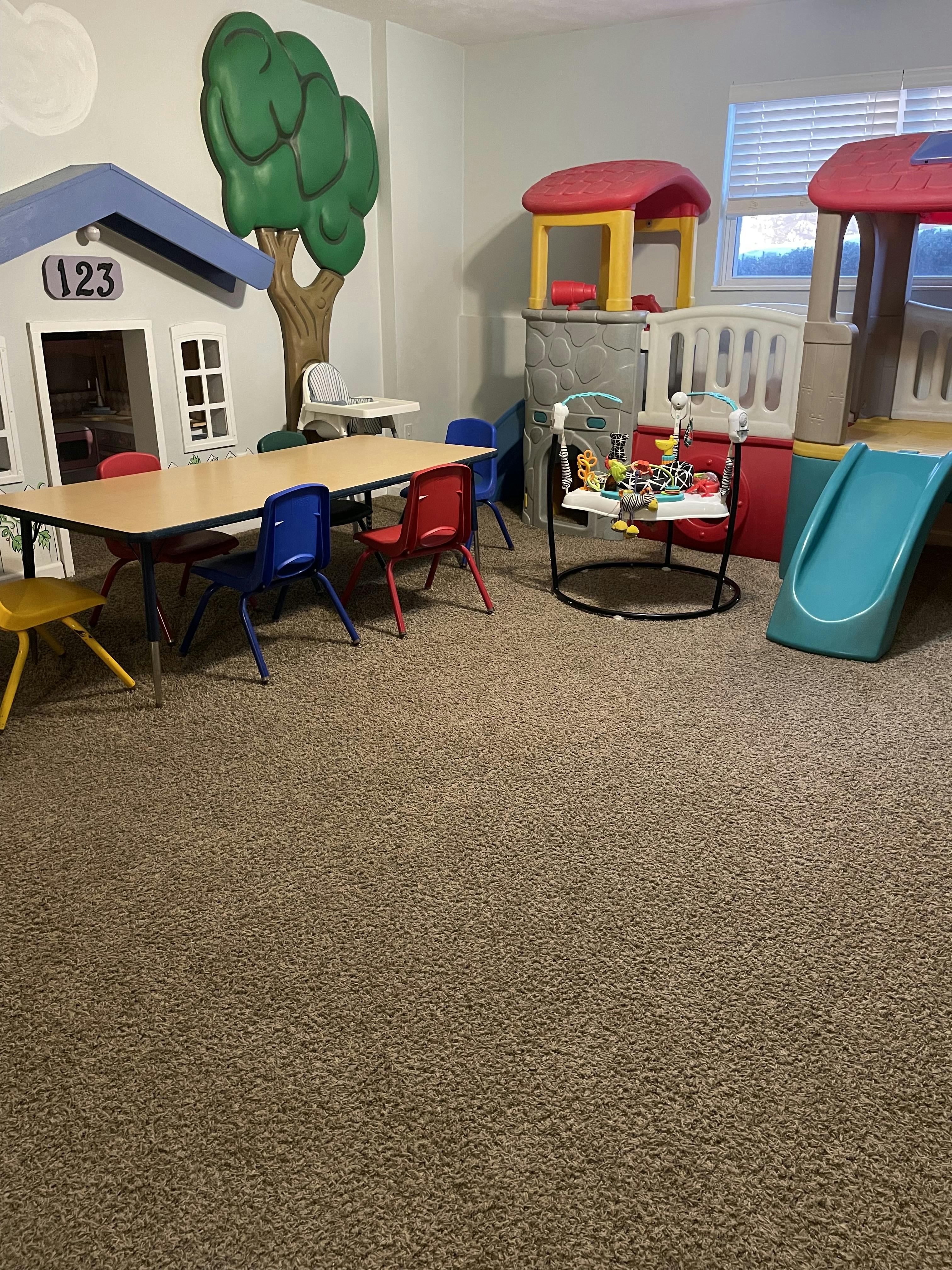 Playroom with a table and chairs, a baby bouncer, and small playhouses with a slide