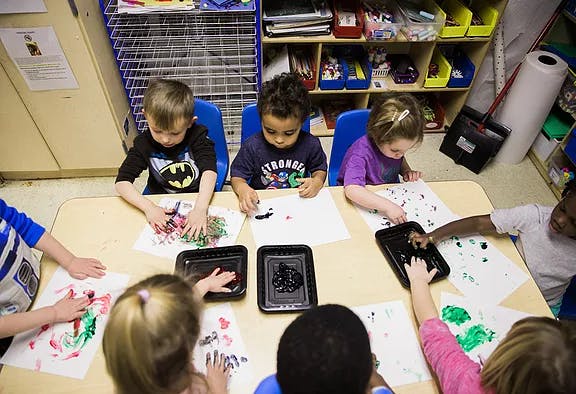 Children finger painting at a table in a classroom