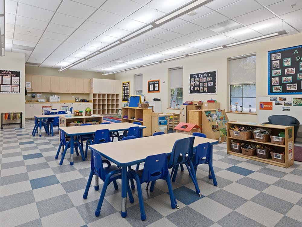 Classroom with small tables, blue chairs, storage cubbies, and various learning materials
