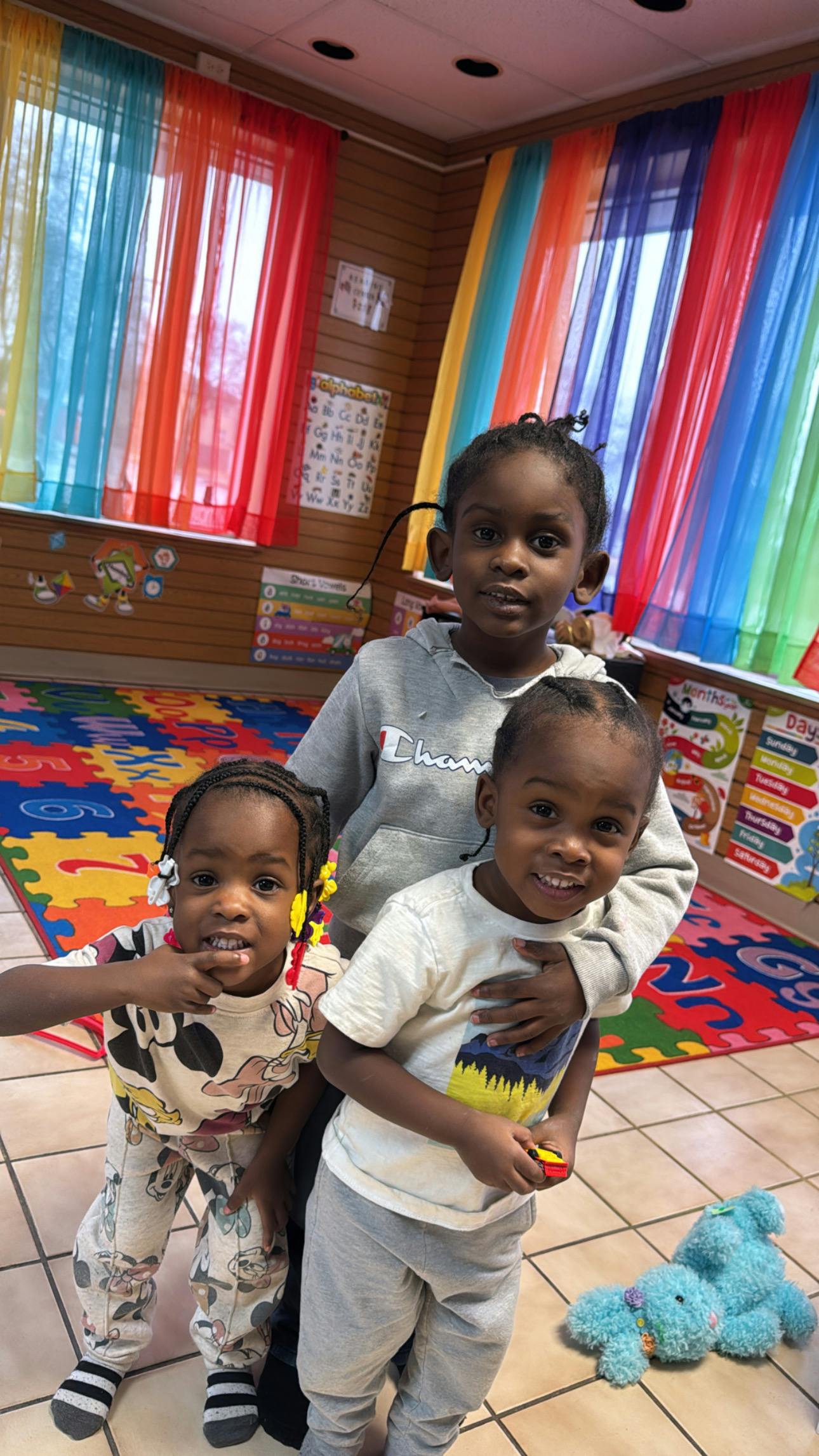 Three children standing together in a brightly decorated classroom
