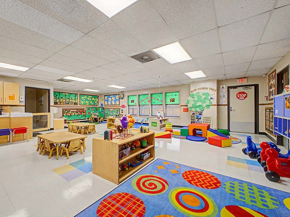 Colorful playroom with small tables, shelves of toys, and padded play equipment