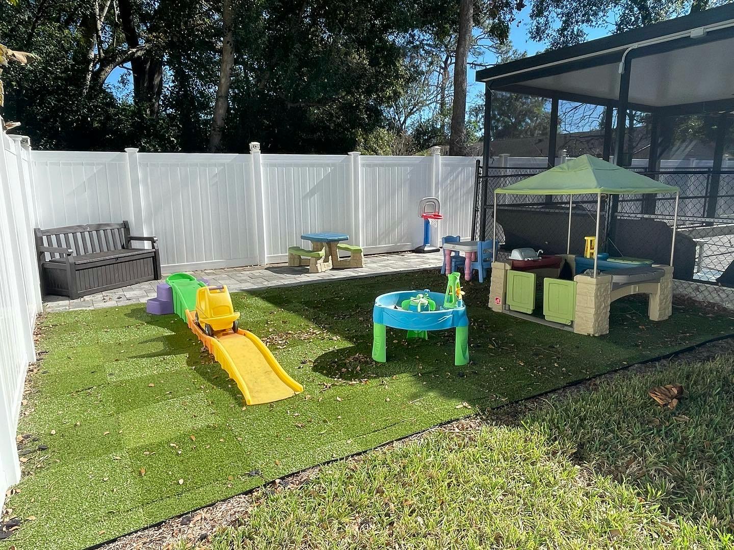 Outdoor play area with a yellow slide, water table, and shaded activity table