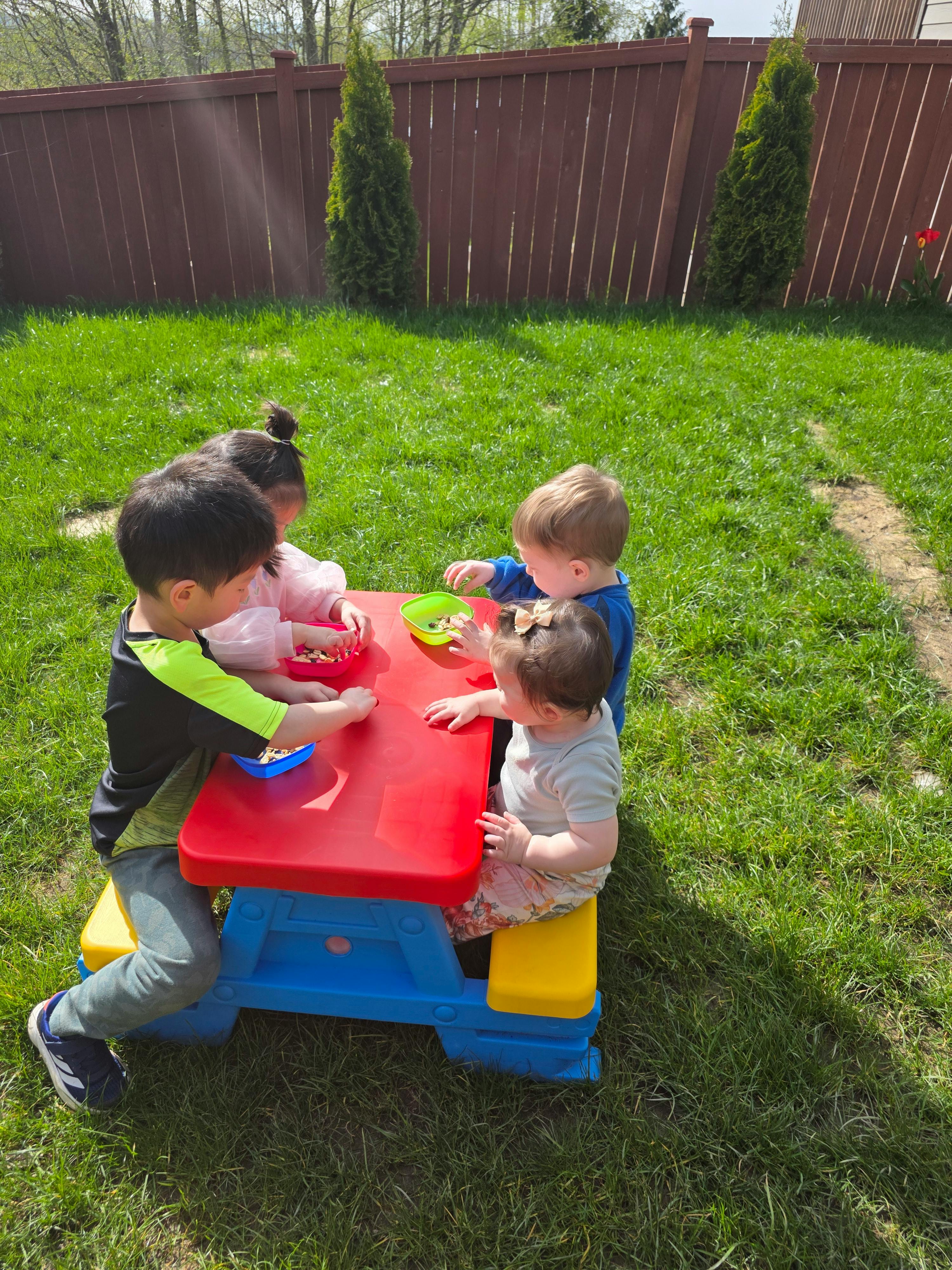 Four children sitting at a small picnic table outdoors