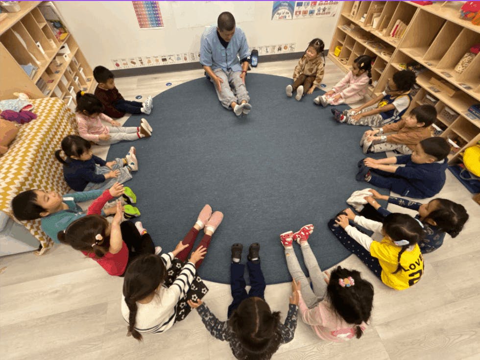 Person and children sitting in a circle on a rug in a classroom