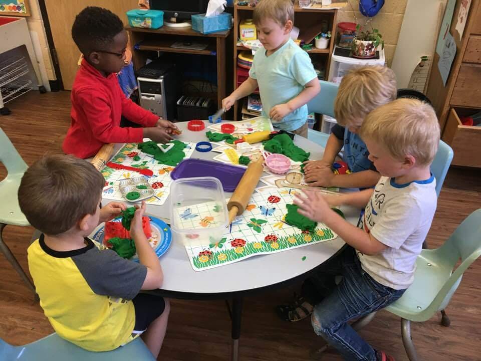 Children playing with modeling clay at a table in a classroom