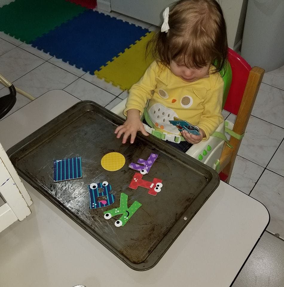 Child in high chair playing with letter magnets on a baking sheet