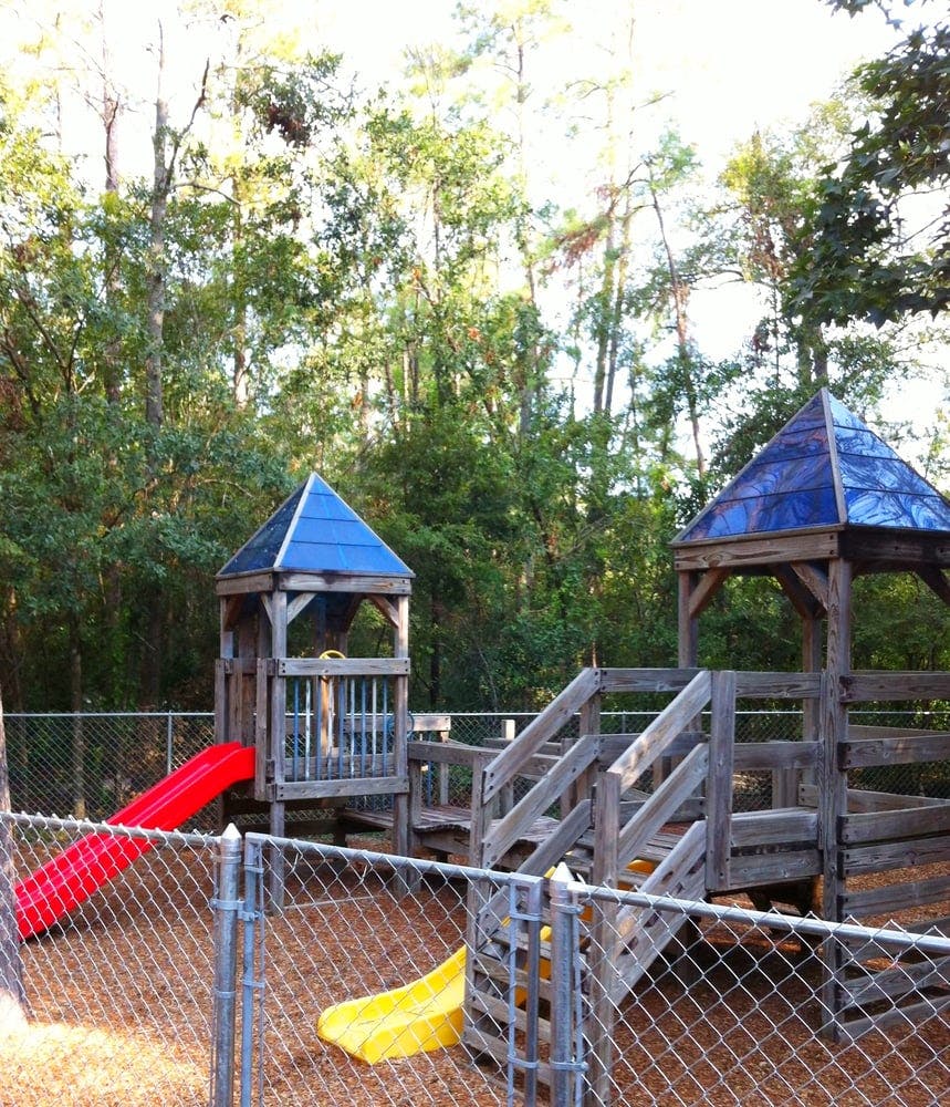 Playground with wooden structures, red slide, and yellow slide behind a fence