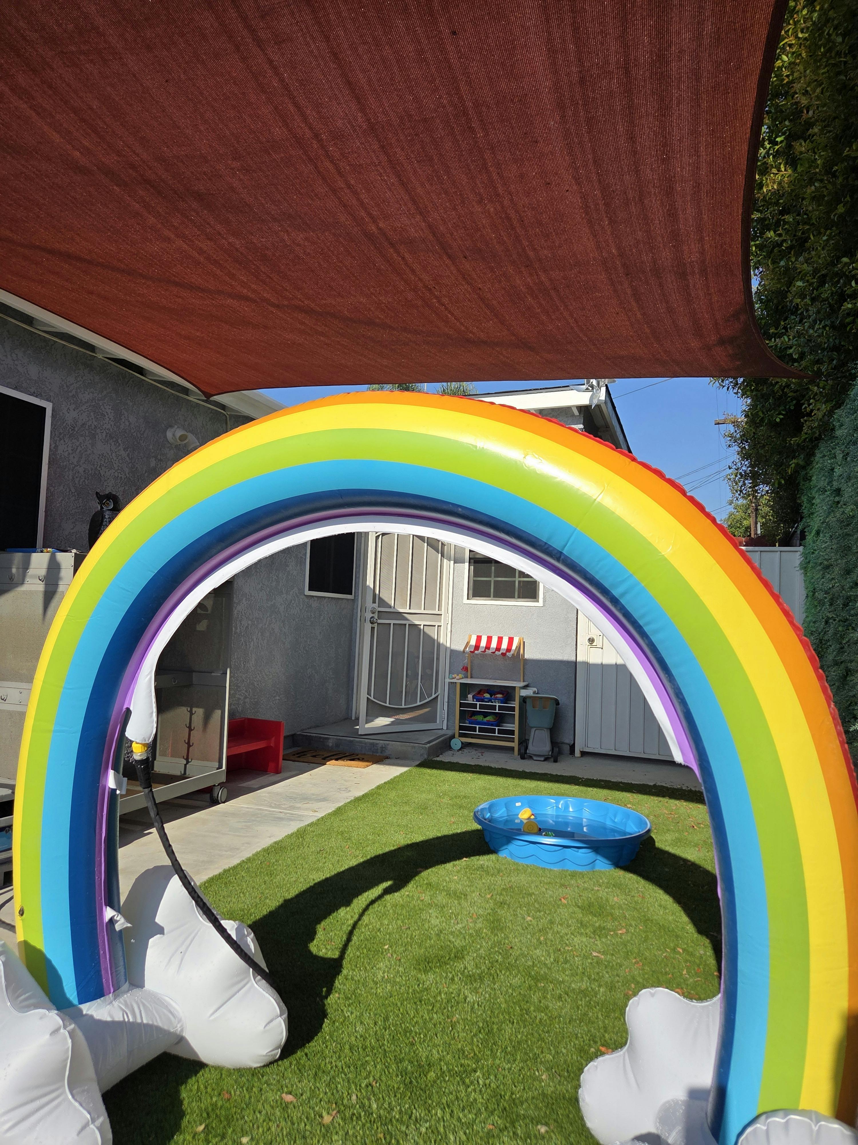 Inflatable rainbow arch over a grassy yard with a small blue pool