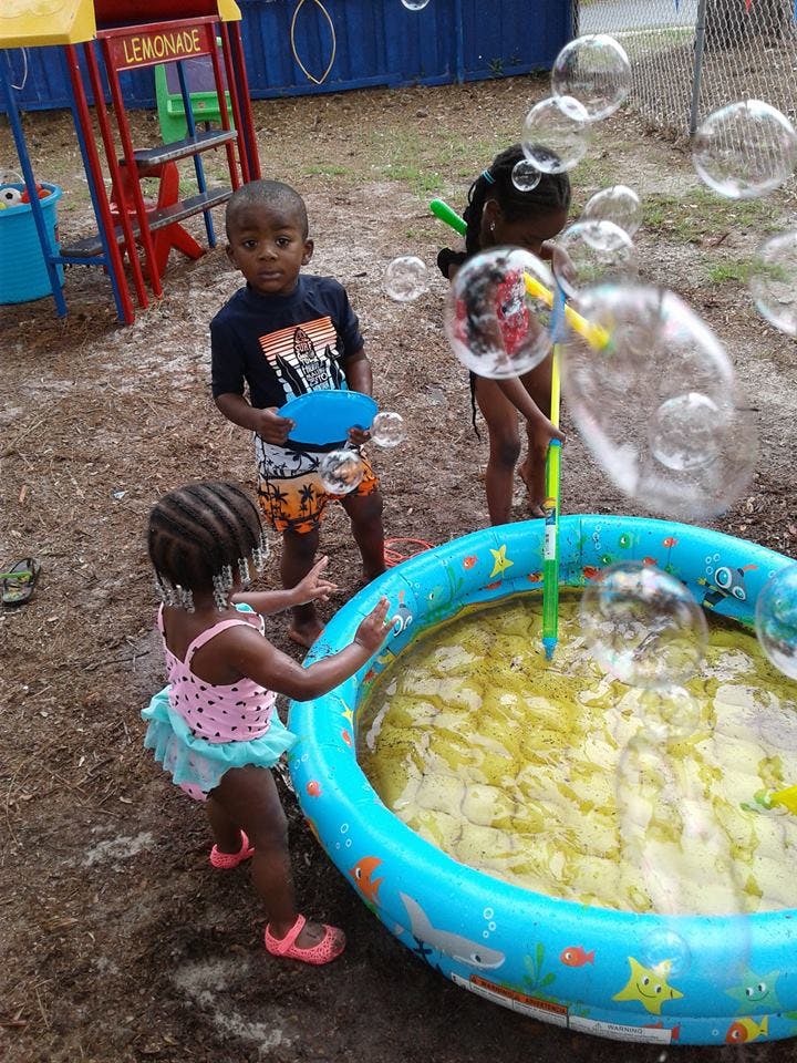 Three children playing with bubbles and a small inflatable pool outdoors