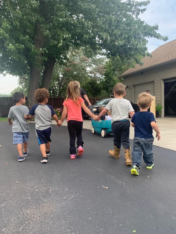 Five children holding hands and walking down a driveway