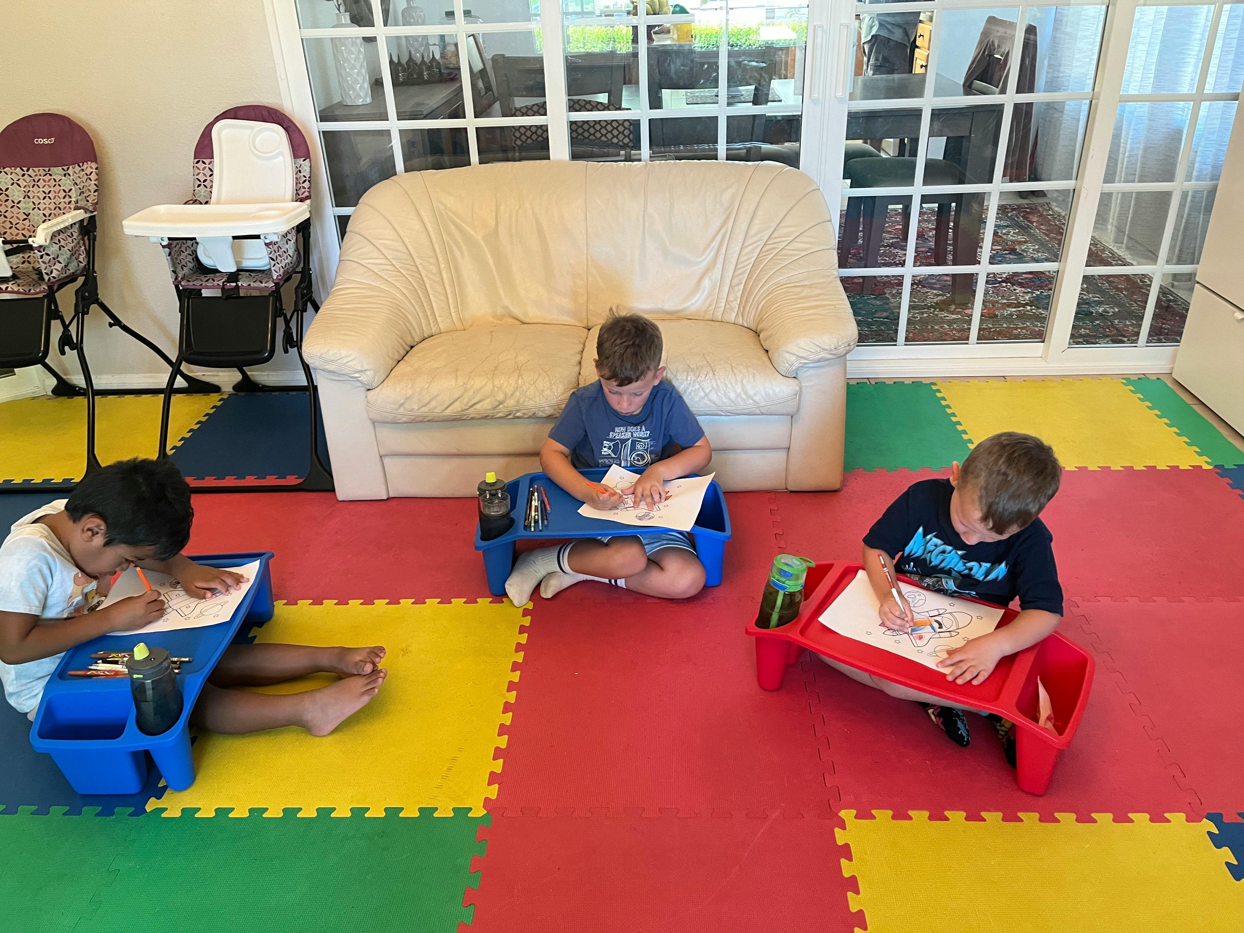 Three children drawing on lap desks on a colorful floor