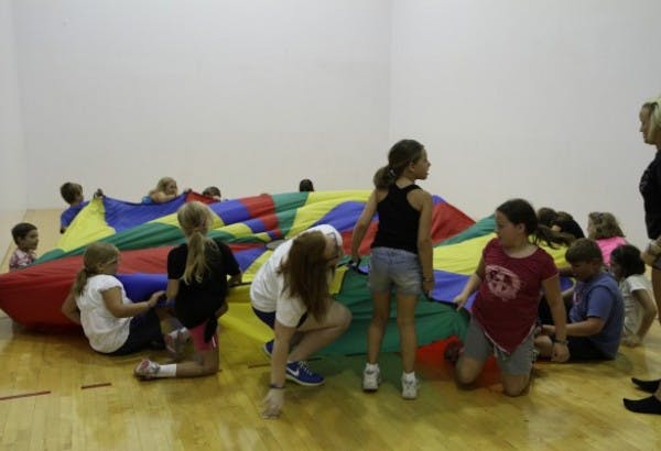 Children playing with a colorful parachute on a wooden floor