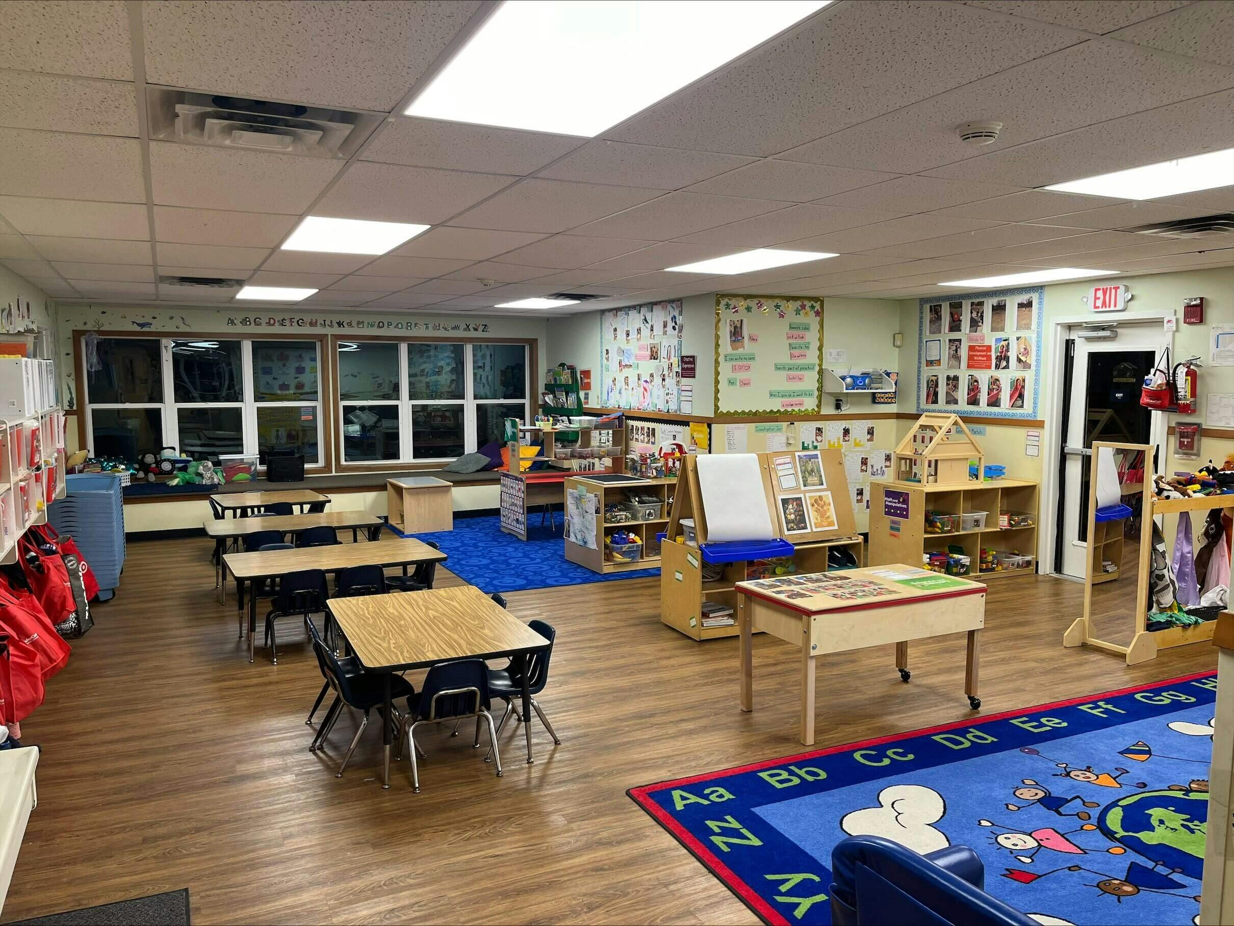 An empty classroom with small tables and chairs, toys, and educational posters