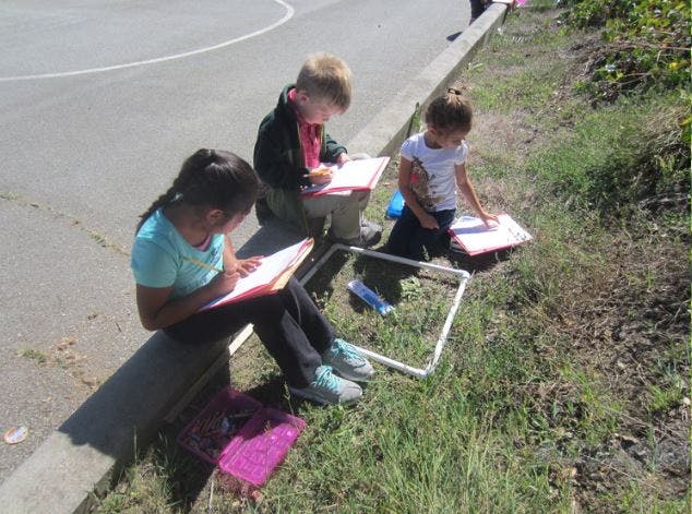 Three children drawing or writing outdoors