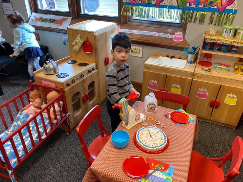 Child standing at a play table with toy food in a classroom