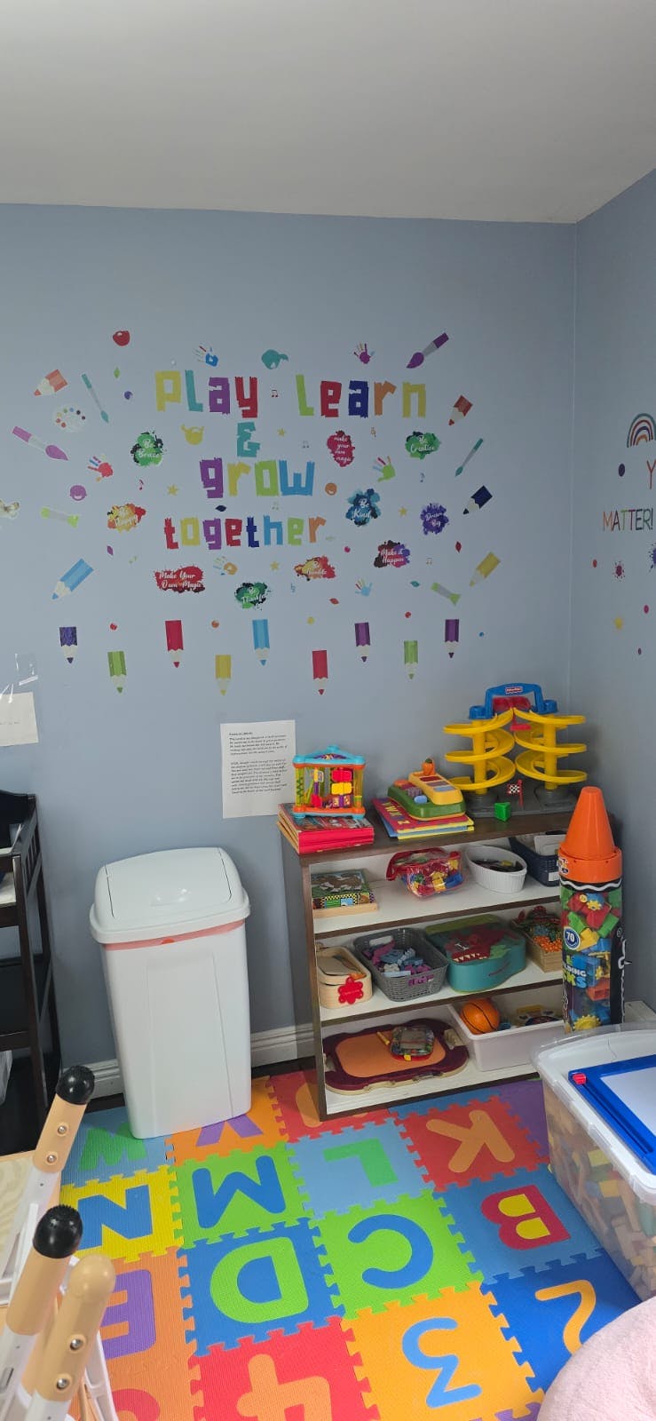 Children's playroom with ABC floor mats and a wall decal saying "Play Learn & Grow Together"