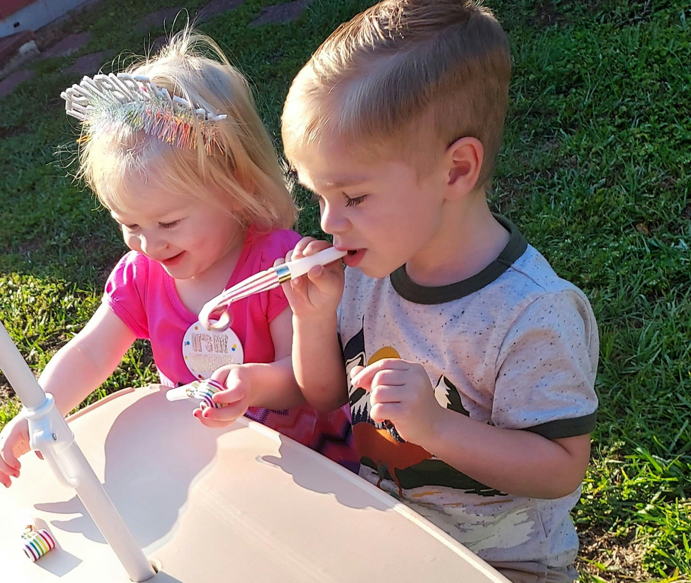 Two children playing with party blowers outdoors