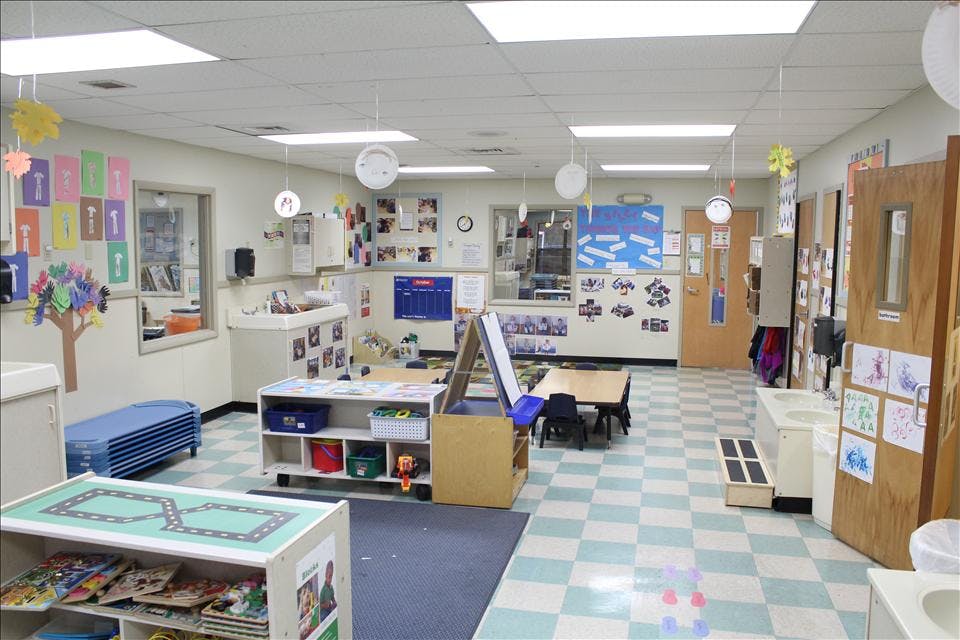 Empty classroom with small tables and chairs, shelves with toys, and artwork on walls