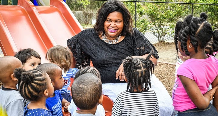 Person sitting on ground surrounded by children on a playground