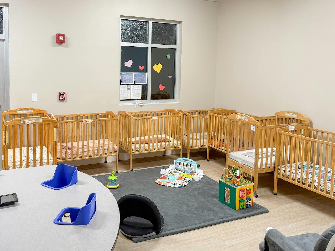 Cribs lined up in a daycare nursery with a floor play mat and toys