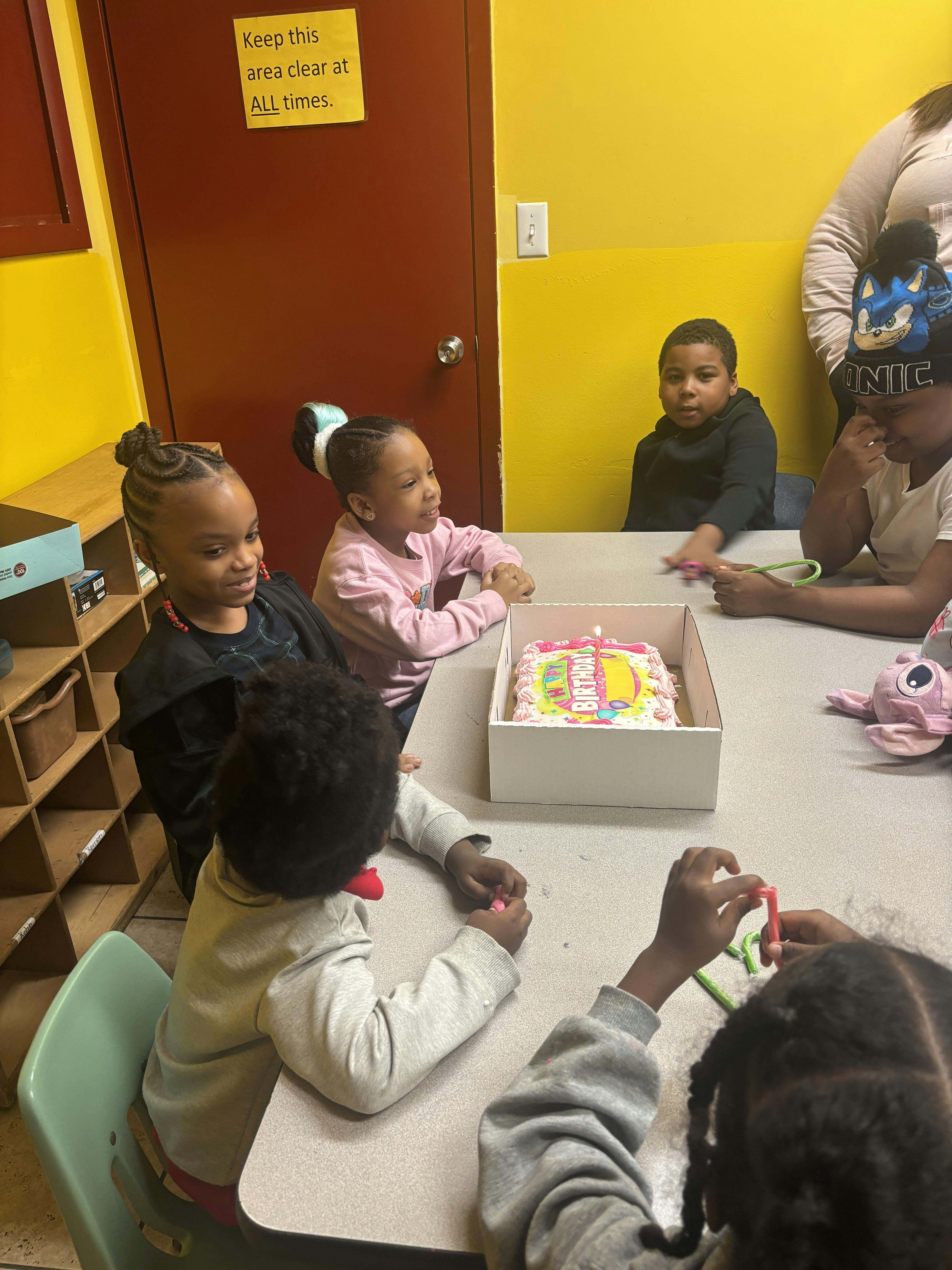 Children gathered around a table with a birthday cake in a box