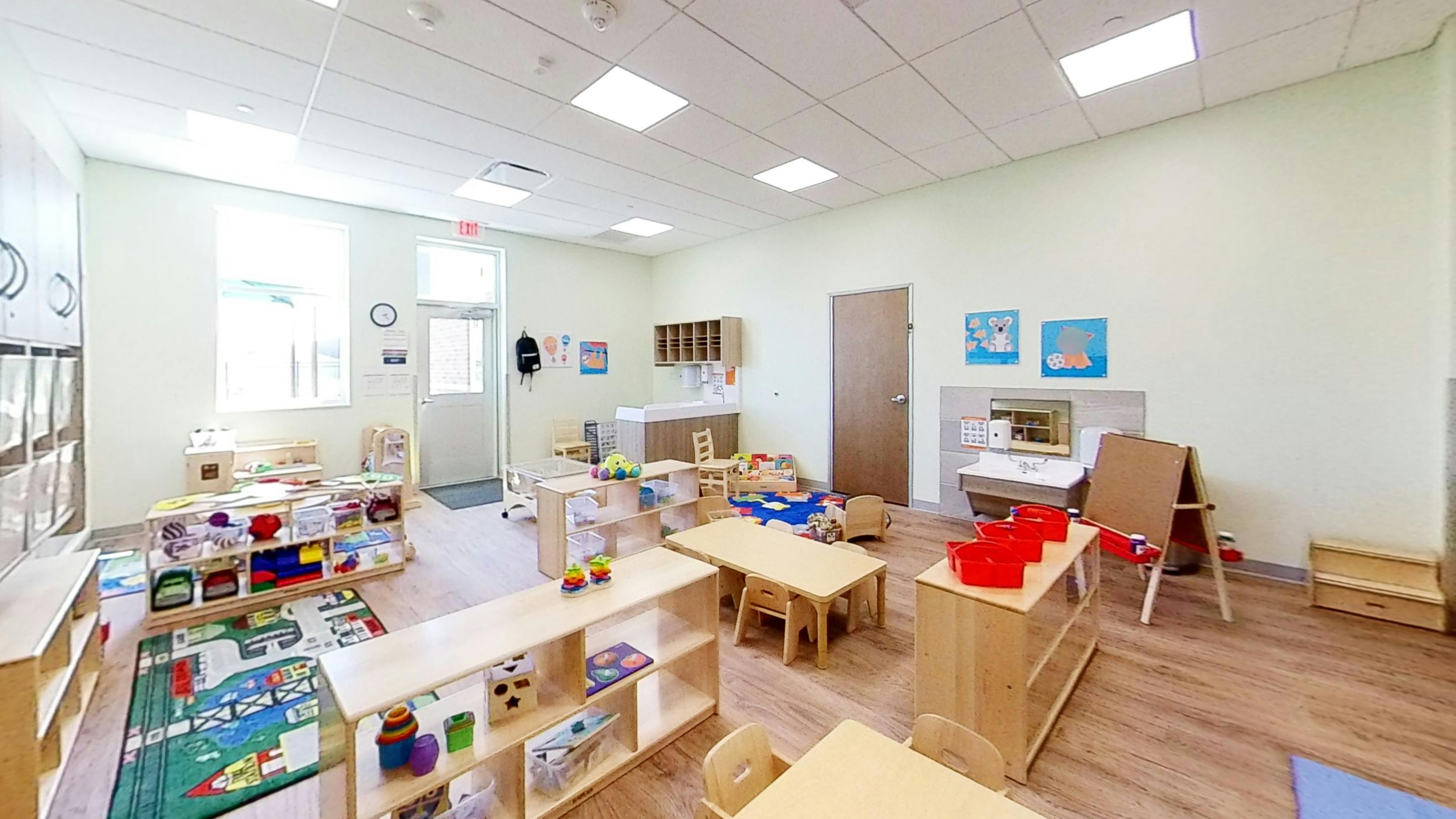 An empty early childhood classroom with small tables, chairs, and play areas