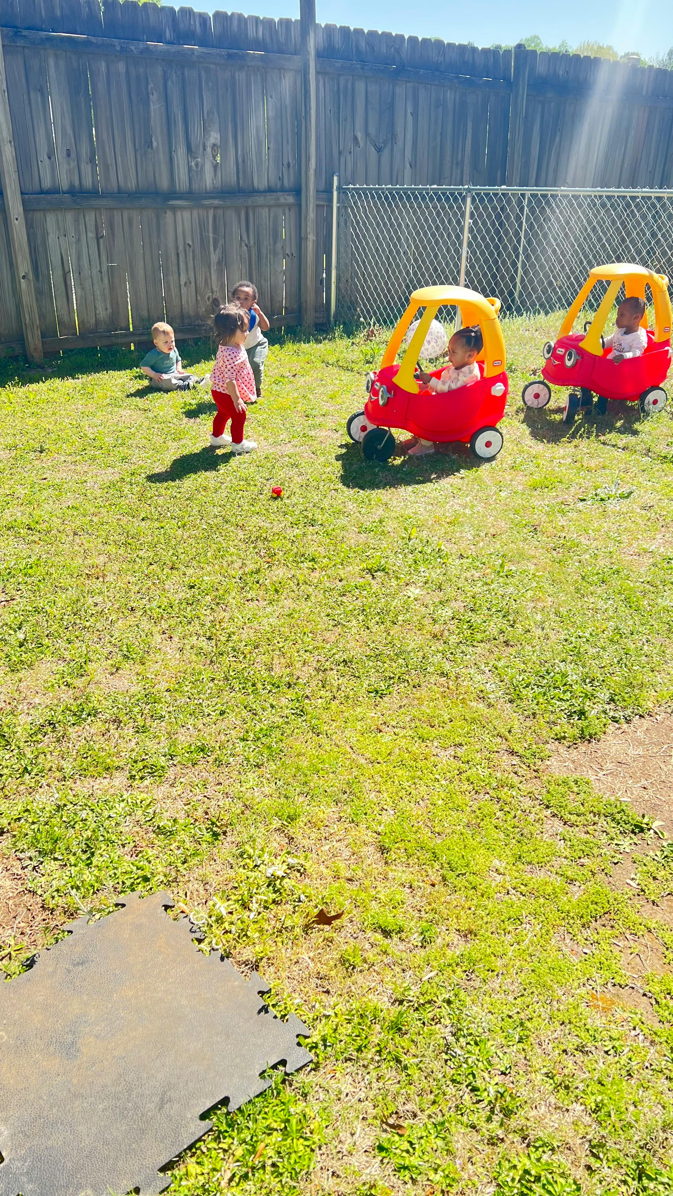 Children playing in a grassy yard with toy cars