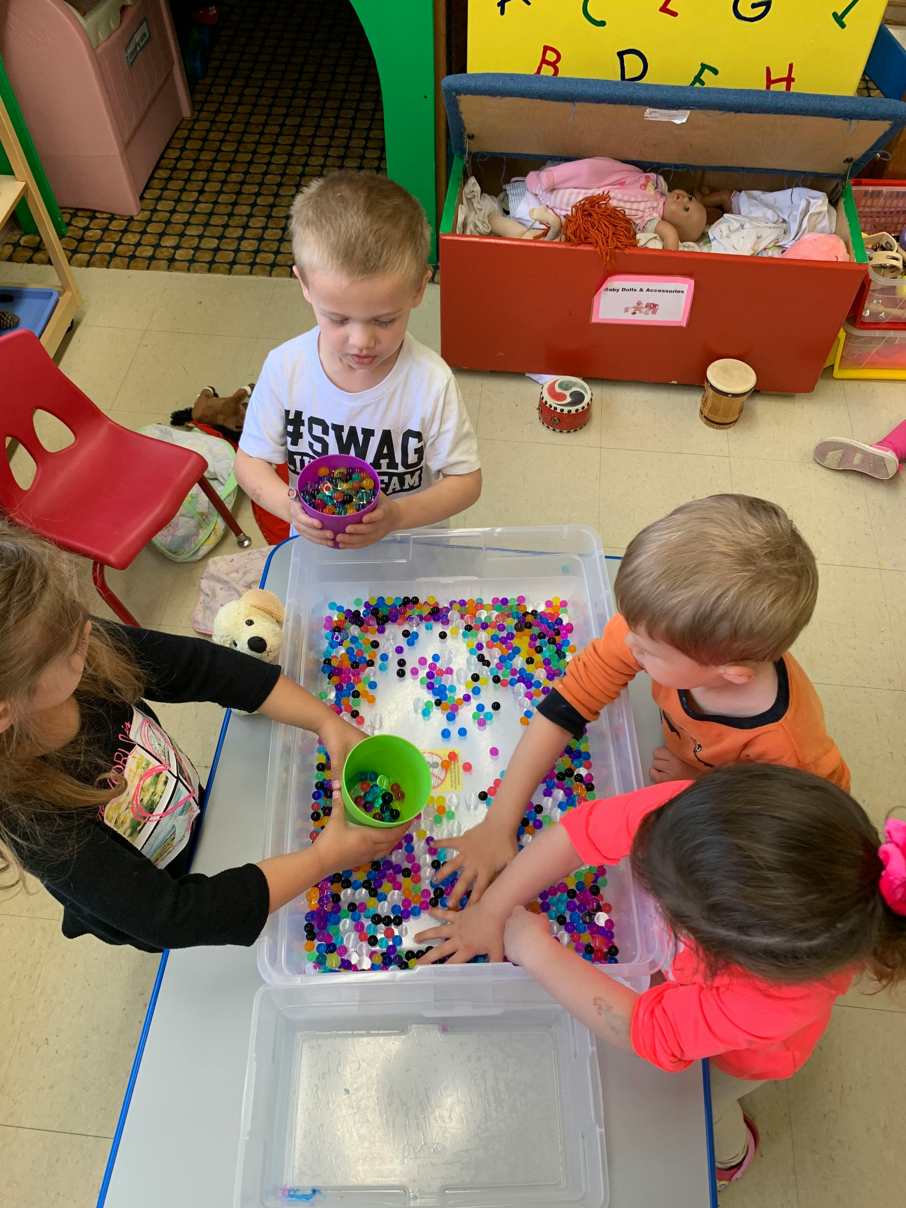 Children playing with colorful beads in a clear container