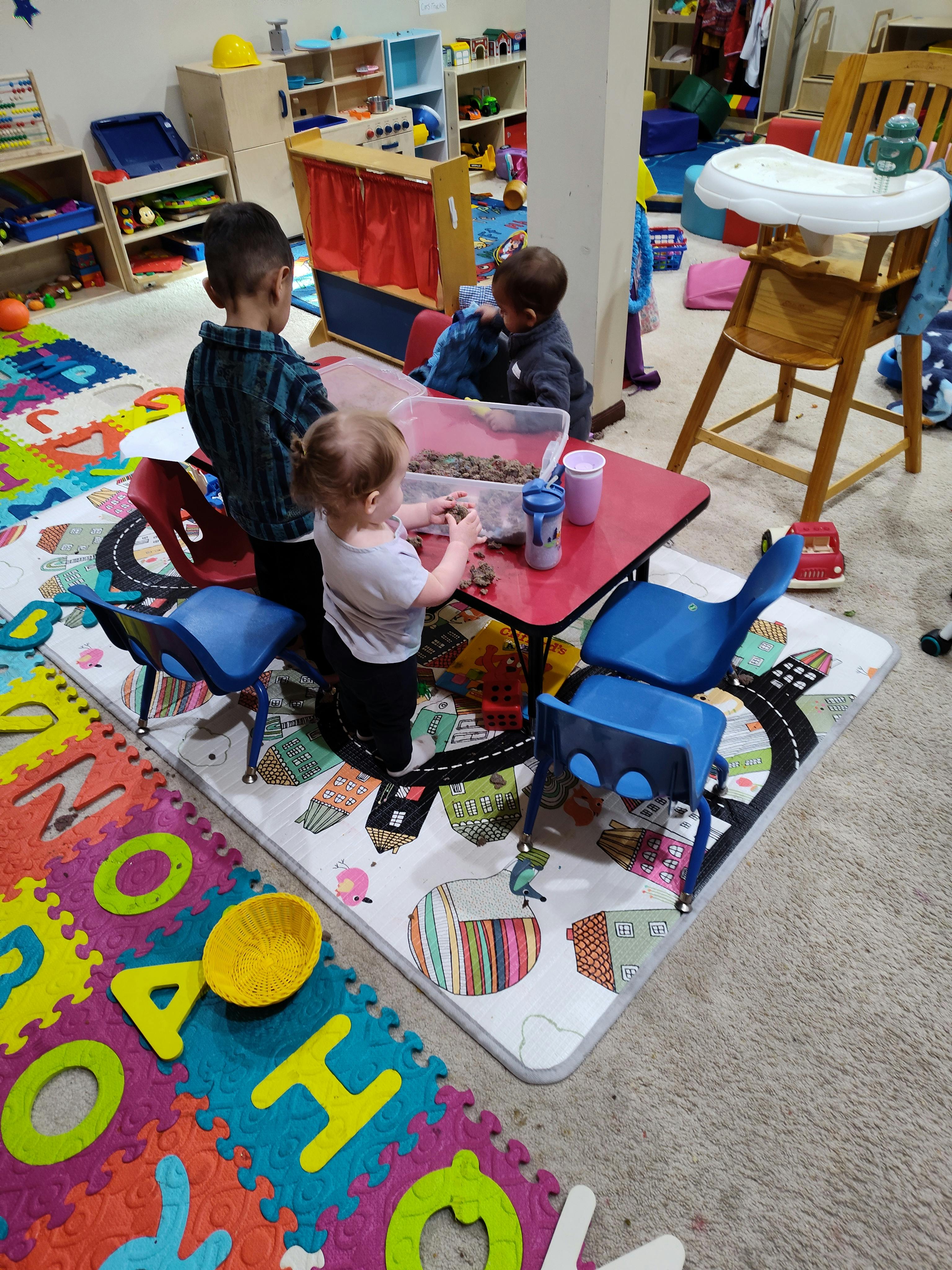 Children playing with kinetic sand at a small red table in a classroom