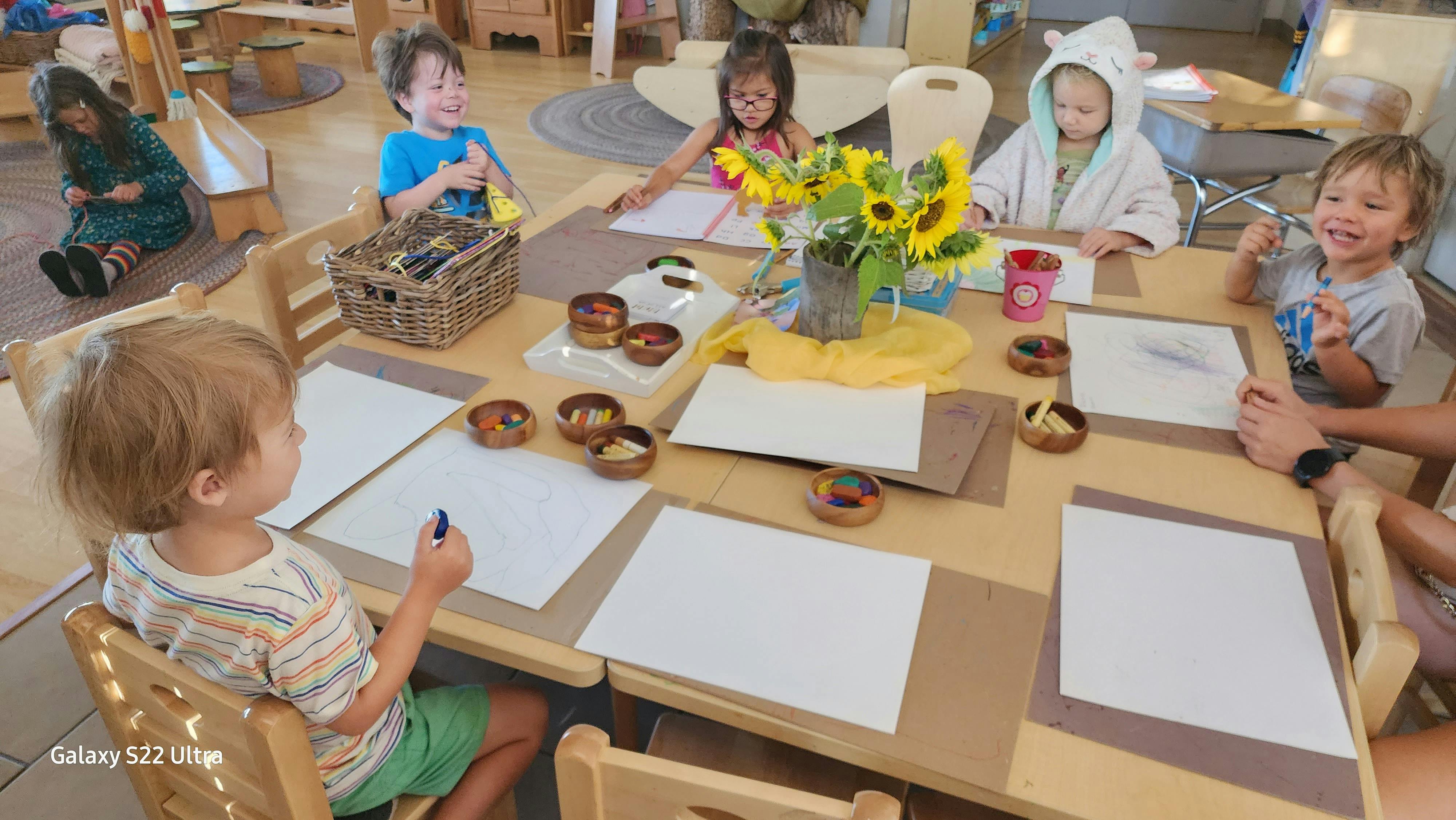 Children sitting at a table with paper and art supplies